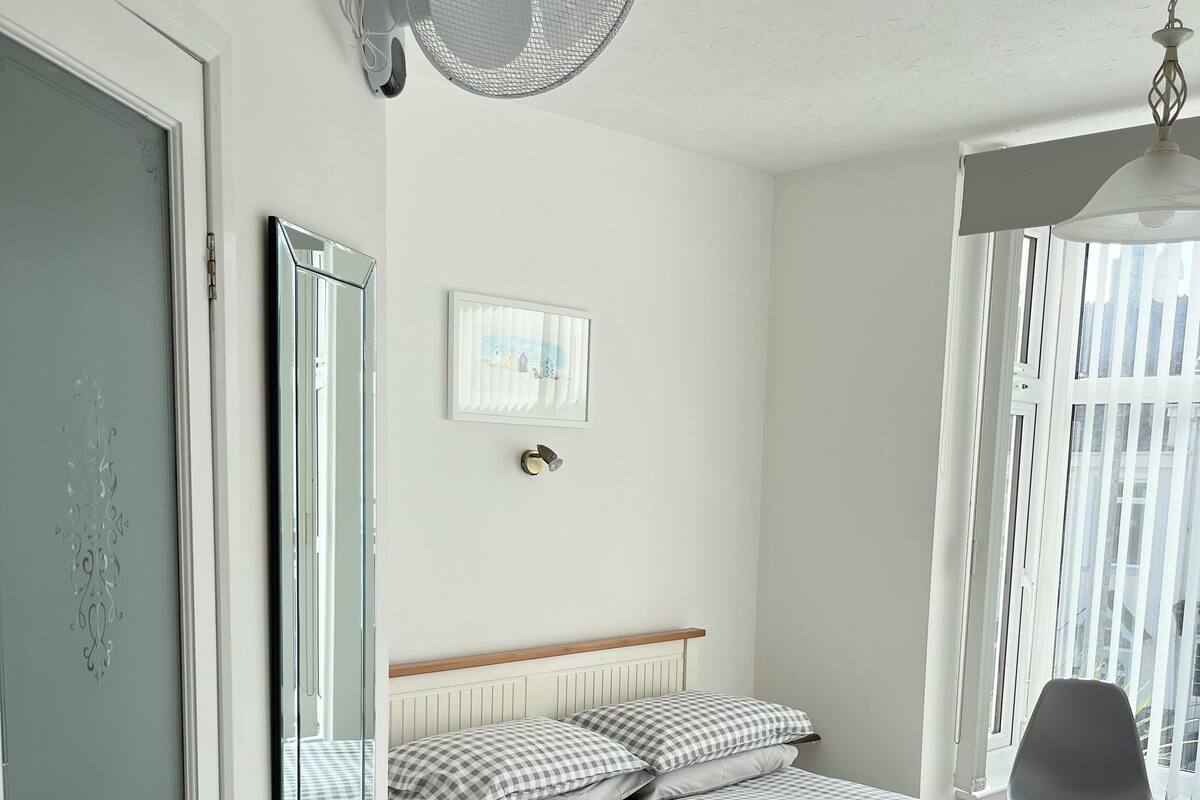 A neatly arranged bedroom with a bed, a bedside table, a chair, a window, and a wall-mounted fan.