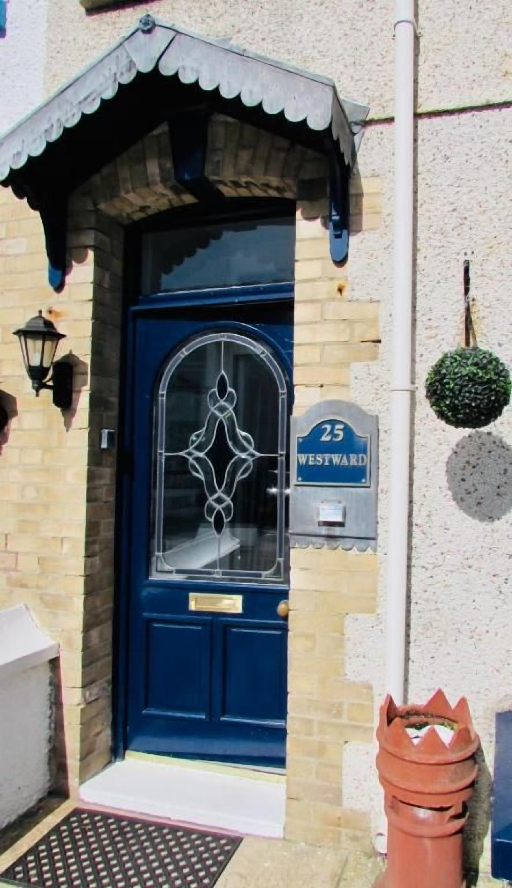A blue door with a number '25' and 'WESTWARD' sign, a small porch with a white trim, and a potted plant on the wall.