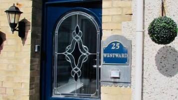 A blue door with a number '25' and 'WESTWARD' sign, a small porch with a white trim, and a potted plant on the wall.
