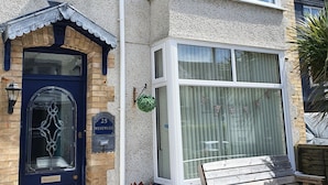 A two-story building with a blue front door, a small garden bench, and a flag decoration. - Westward Bed & Breakfast (Newquay)