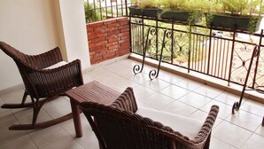 A balcony with wicker furniture, a tiled floor, and a view of greenery through a metal railing. - Aparta Hotel Turey (Santo Domingo)