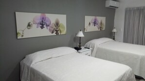 A hotel room with two beds, a nightstand with a lamp, and two wall-mounted flower paintings. - Aparta Hotel Turey (Santo Domingo)