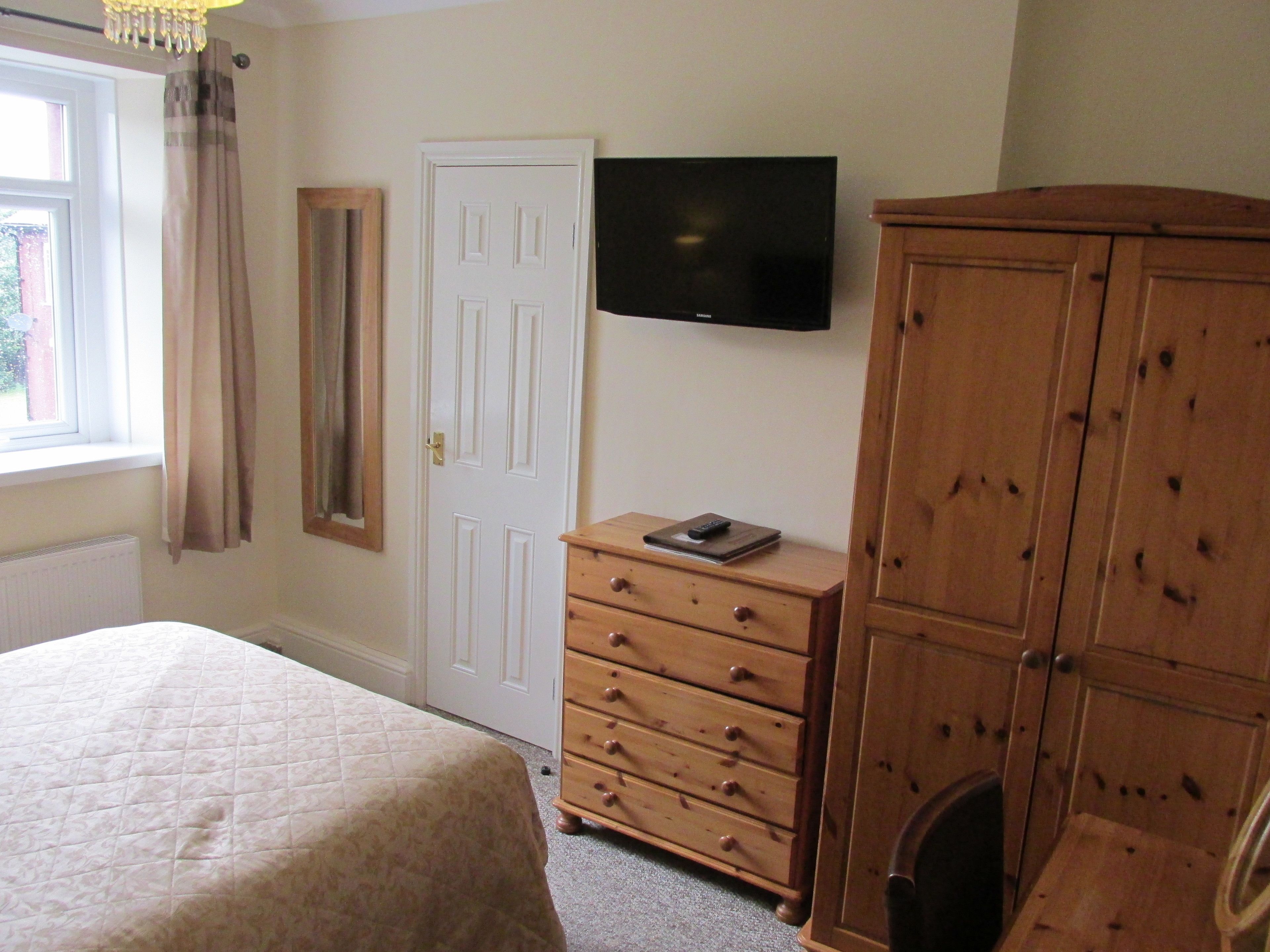 A bedroom with a bed, a dresser, a television on the wall, and a door.