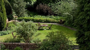 Un jardí ben cuidat amb una paret de pedra, una taula rodona i dues cadires.
