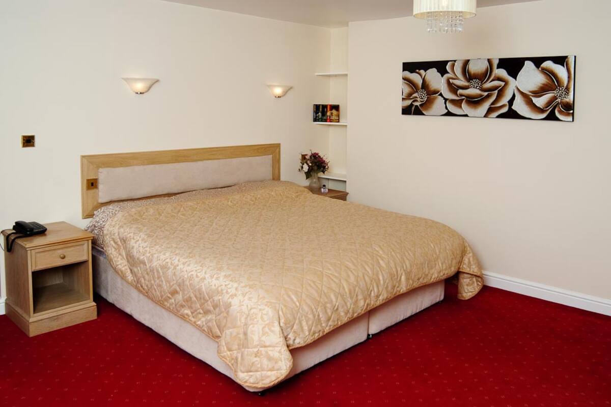 A neatly made bed with a wooden headboard, a bedside table with a lamp, and a floral artwork on the wall.