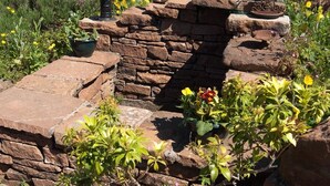 Edifici de pedra amb un petit jardí, incloent una planta en test i plantes de flors.