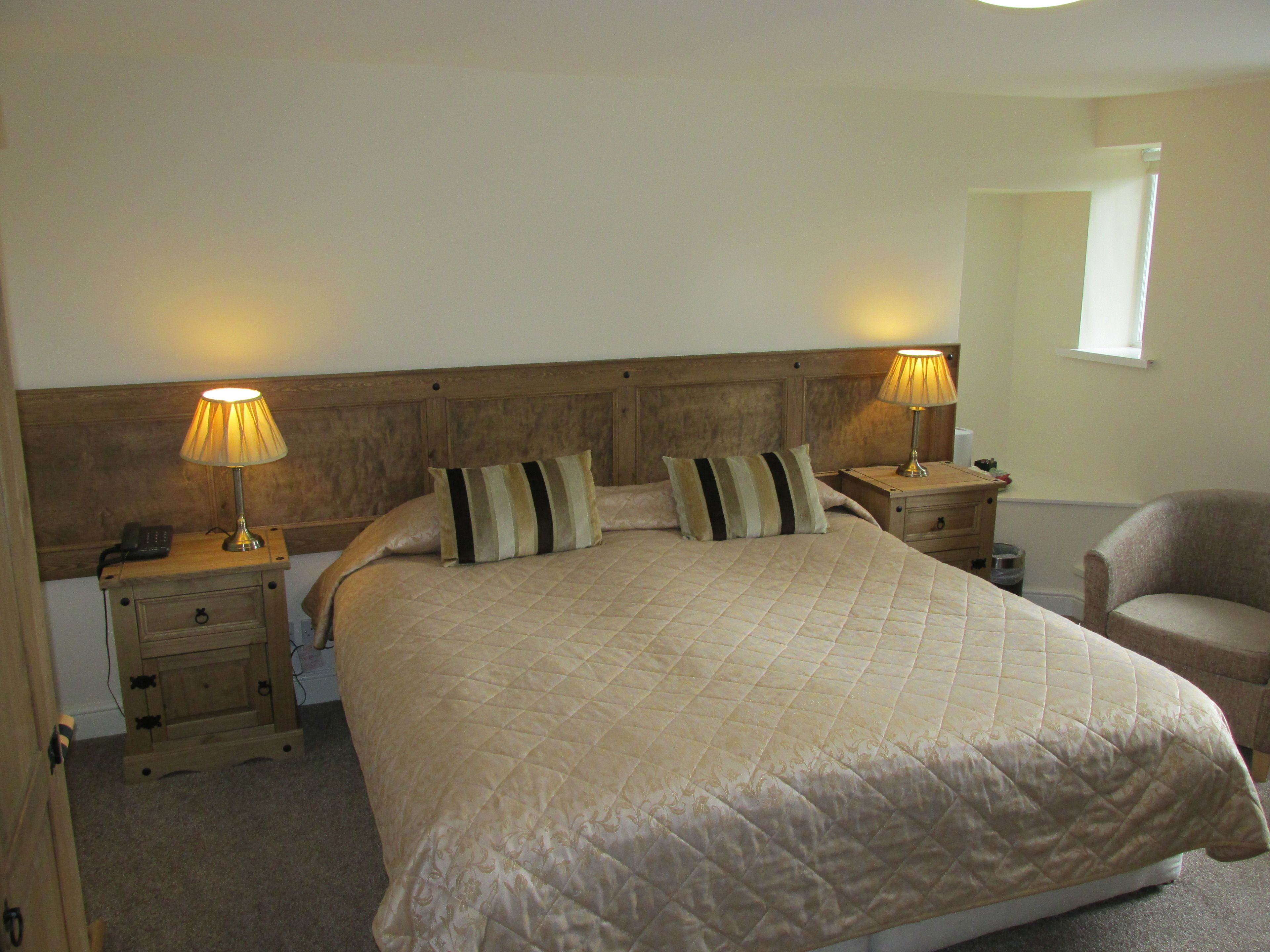 A bedroom with a large bed, two bedside tables with lamps, a chair, and a small window.