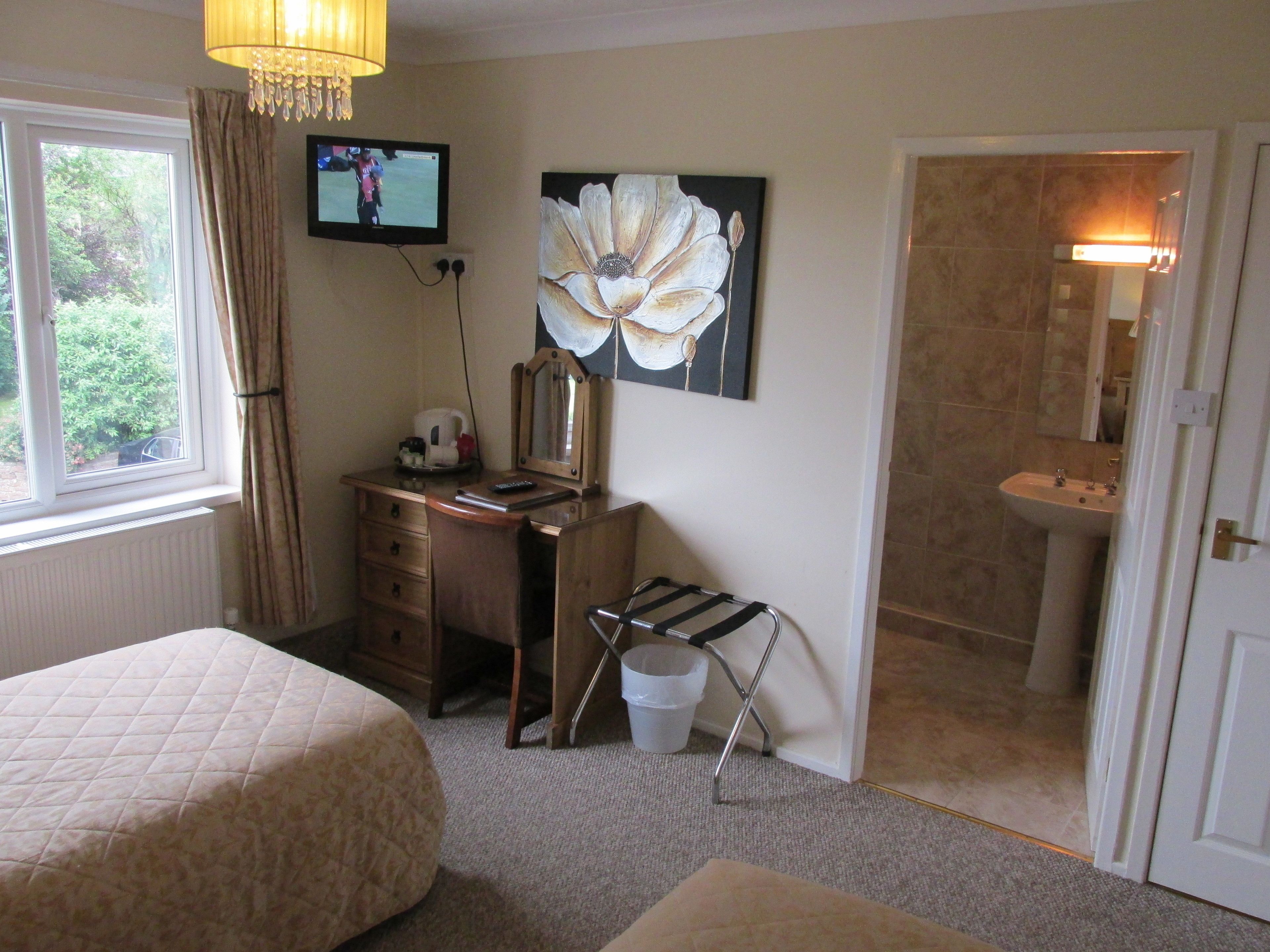 A hotel room with a bed, a desk with a chair, a television, a painting, and a bathroom.