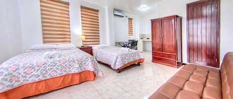 A hotel room with two beds, a desk, a wardrobe, and a sofa.