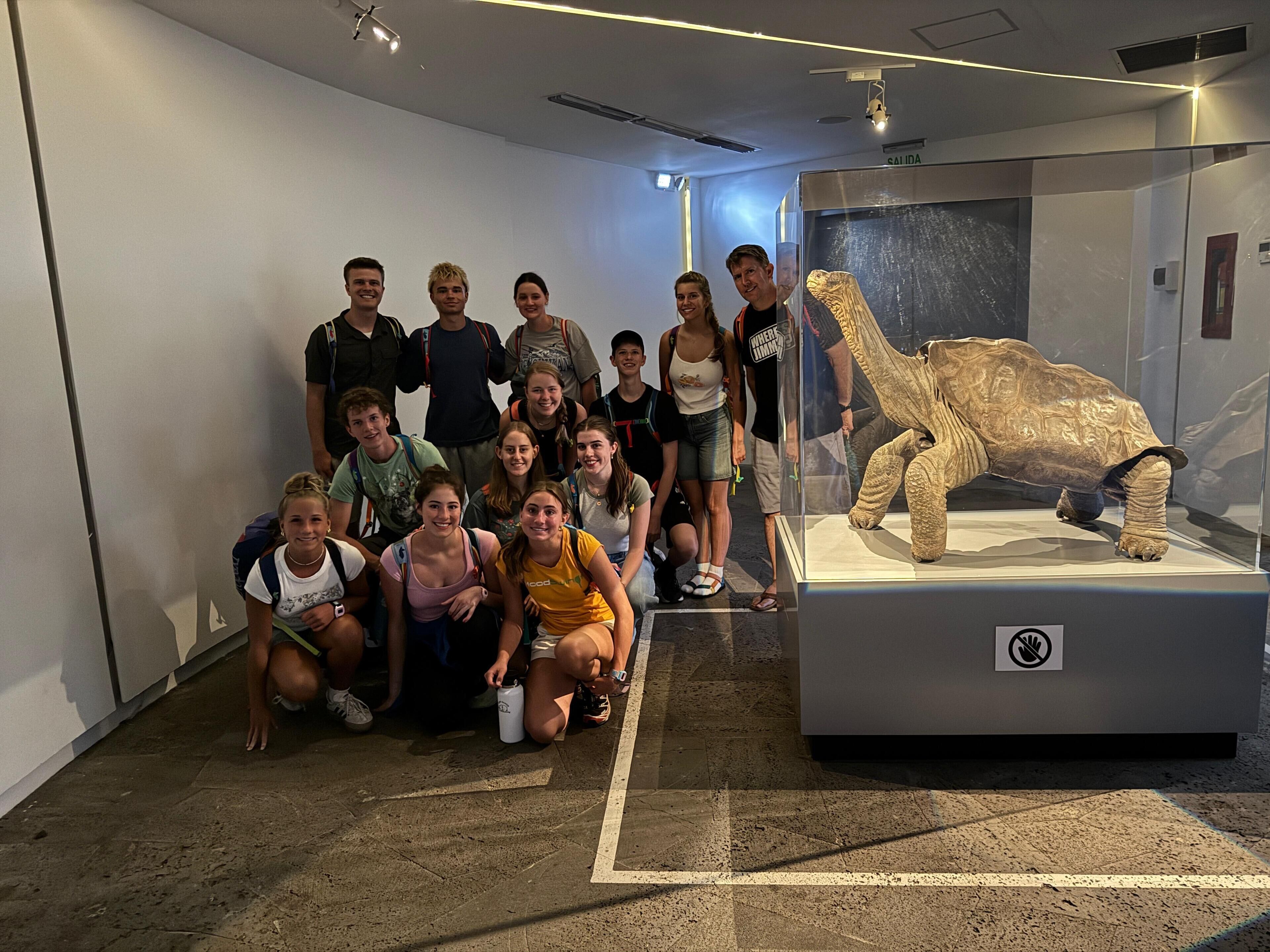 Un grupo de personas en un entorno similar a un museo, con una exposición de dinosaurios.