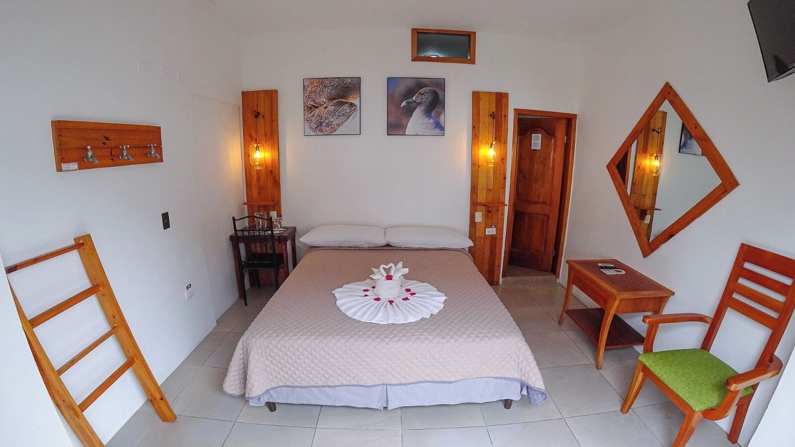 A bedroom with a bed, a wooden chair, a desk, a mirror, and wall-mounted lights.