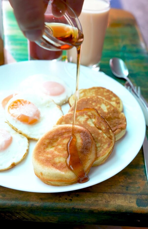 Un plato con panqueques y huevos fritos, y jarabe siendo vertido encima.