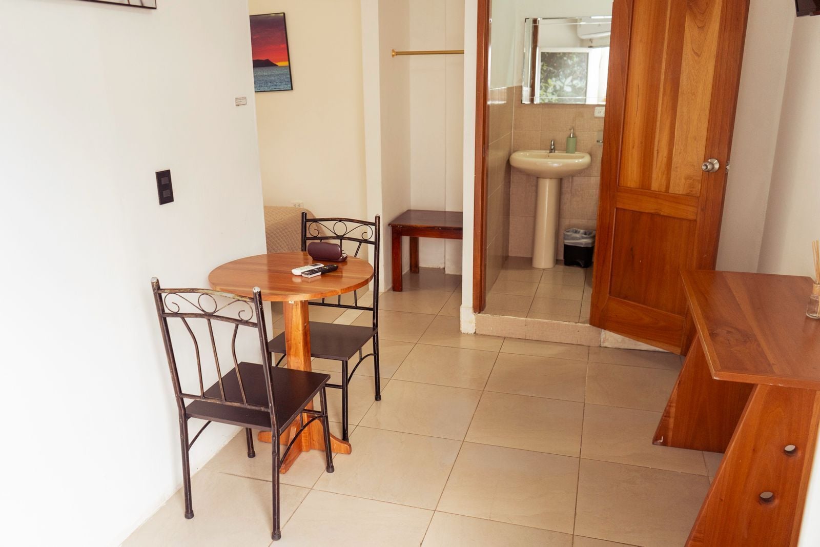 A small dining area with a round table and four chairs, a wooden bench, and a wooden cabinet.