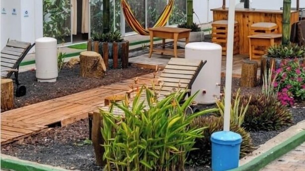 Un espacio al aire libre techado con una hamaca, asientos de madera y plantas en macetas.