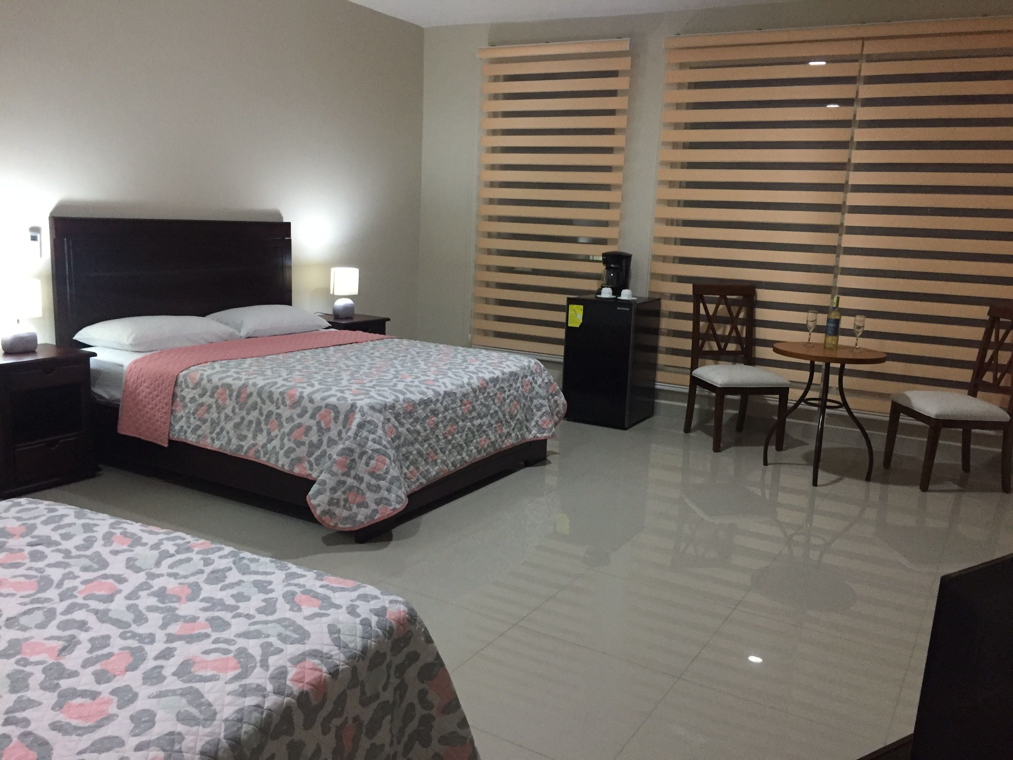 A hotel room with a bed, bedside table, lamp, and a small table with chairs.