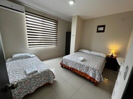Habitación de hotel con dos camas, una ventana con persianas, una mesita de noche con lámpara y un cuadro enmarcado en la pared.
