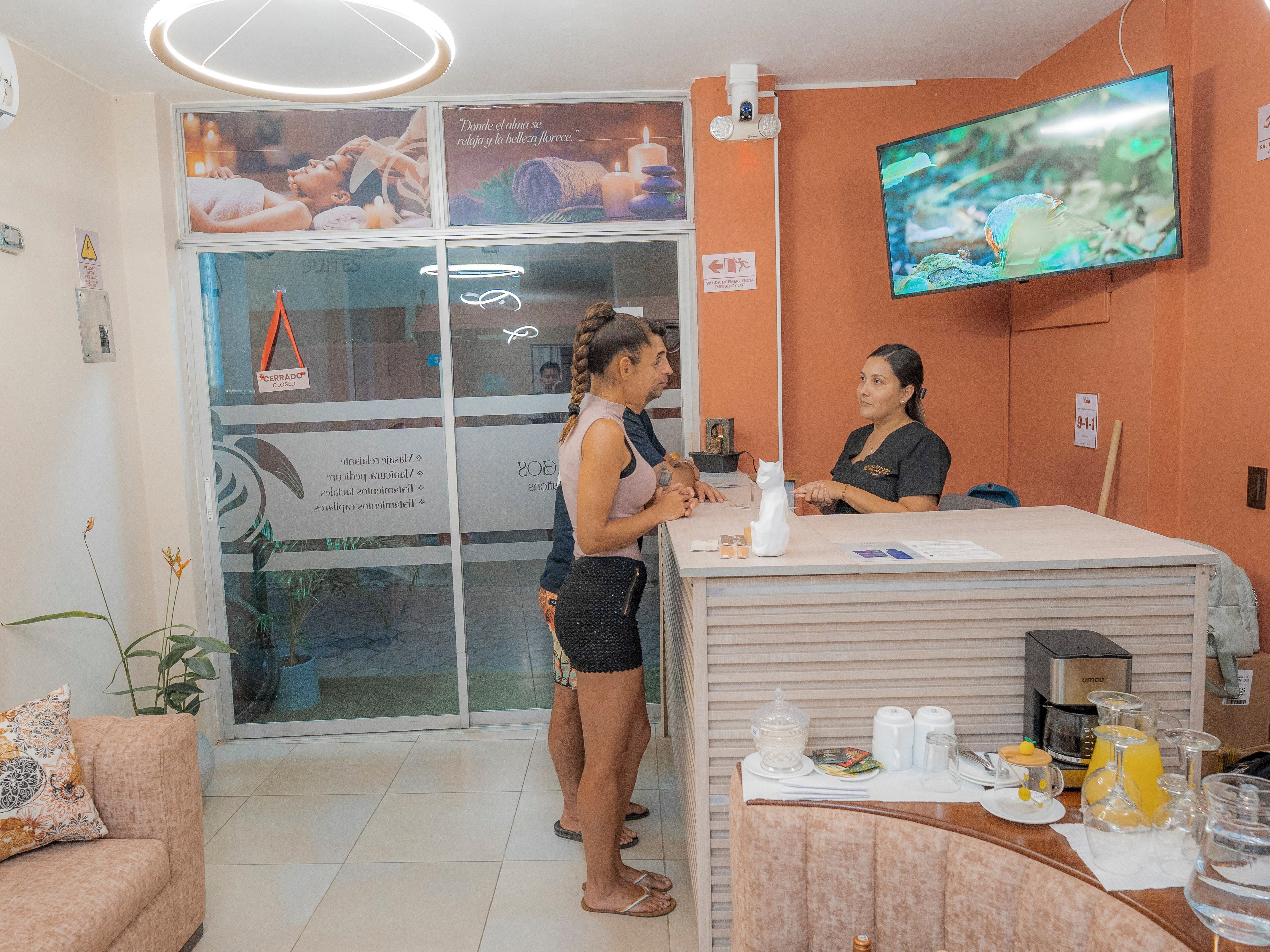 Zona de recepción con mostrador, un televisor montado en la pared y un letrero que indica una salida de emergencia.