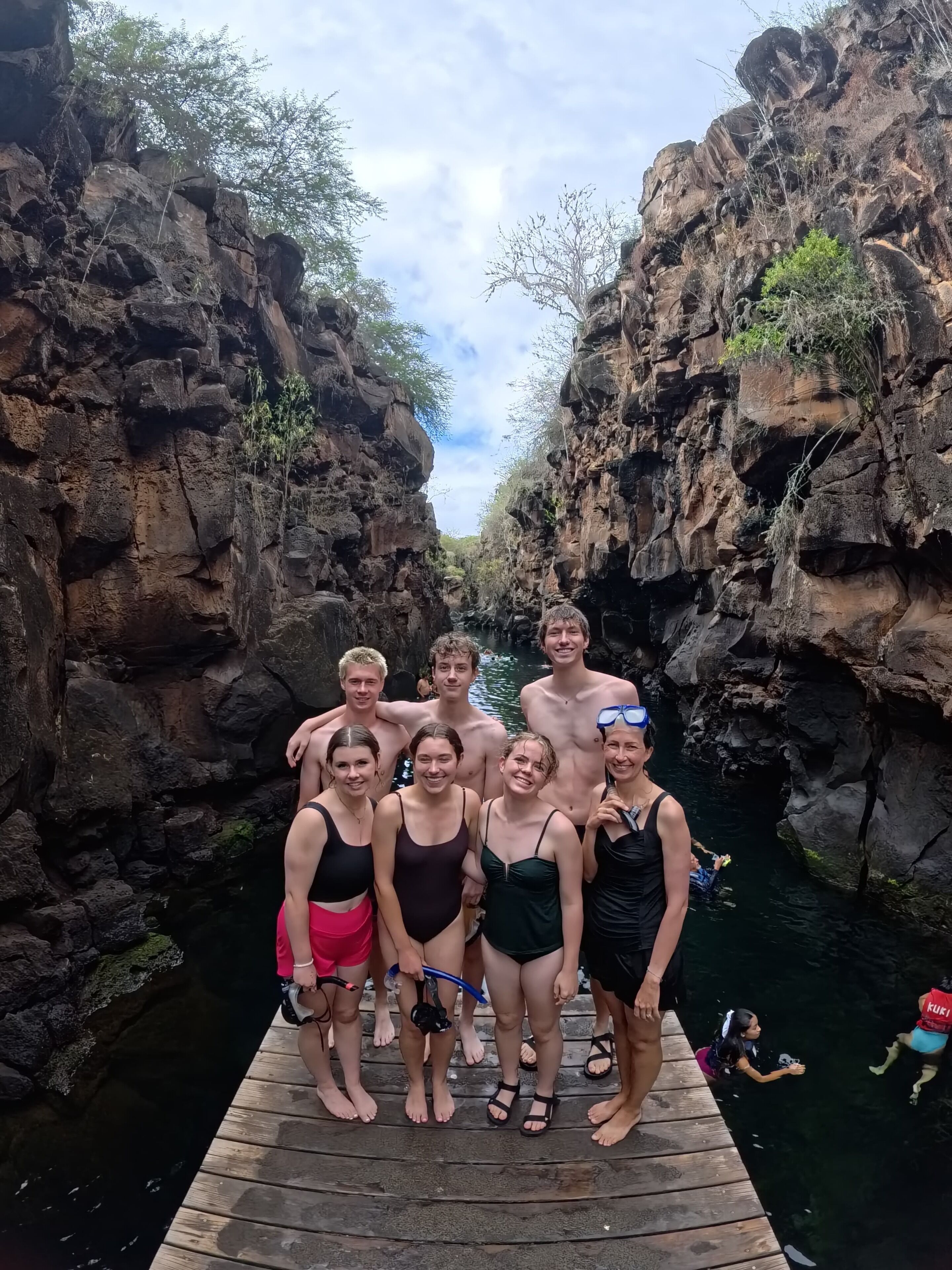 A group of people on a wooden dock by a rocky waterway.