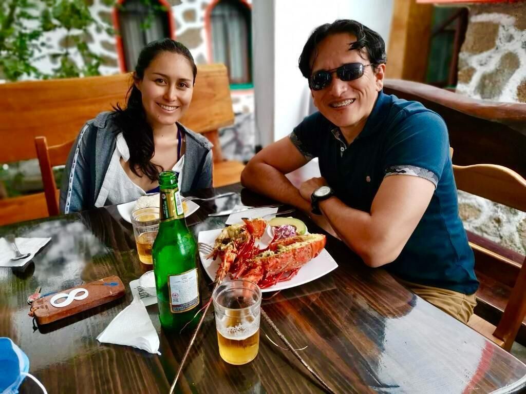 Dos personas sentadas en una mesa con un plato de langosta, una botella de cerveza y un vaso de cerveza.