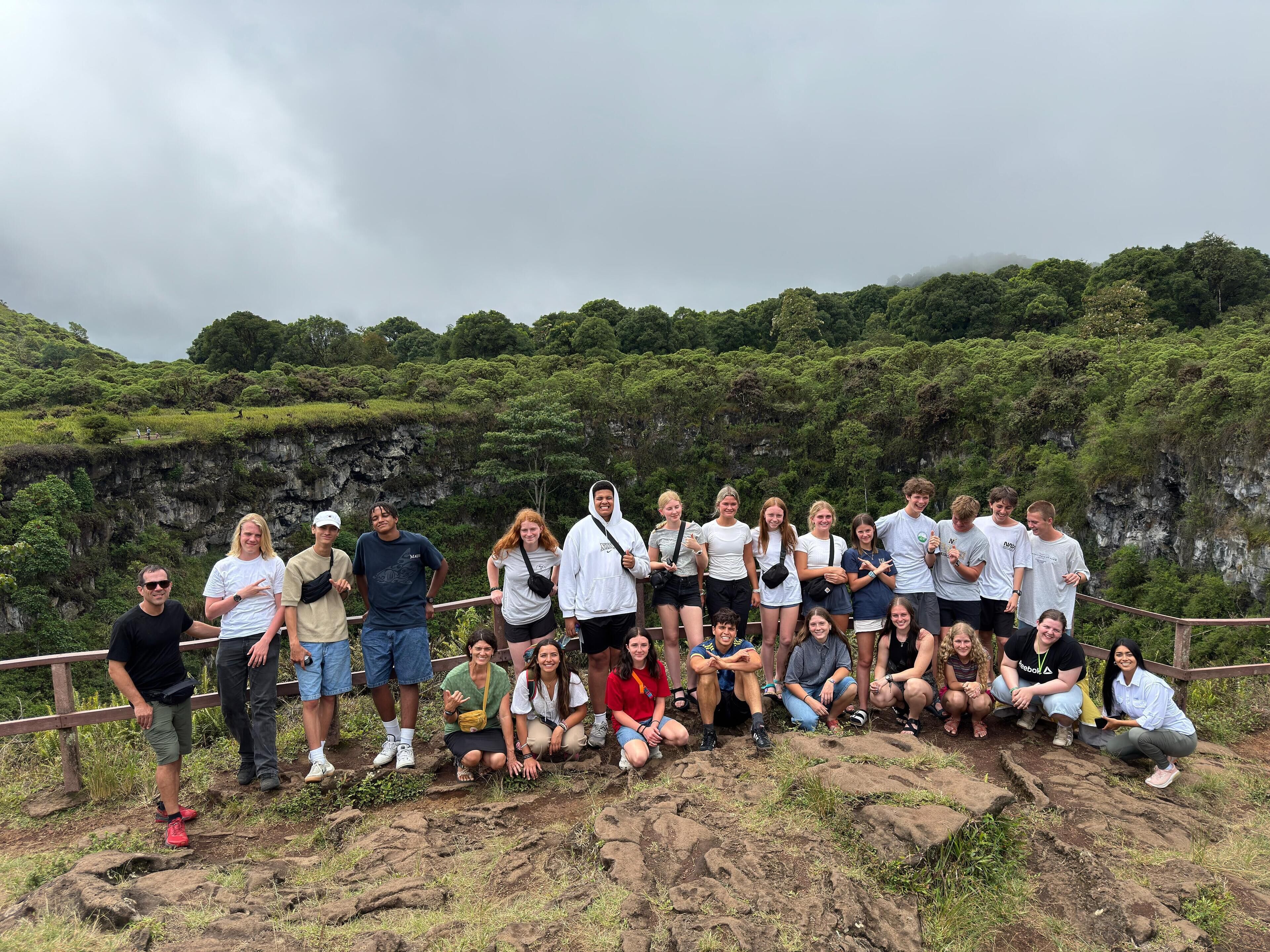 A group of people posing on a rocky outcrop with a forested cliff in the background.
