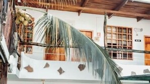 Un edificio de dos pisos con ventanas y puertas de madera, un balcón con una palmera y un letrero que indica el número de habitación.