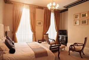 A hotel room with a large bed, two chairs, a television, and a dresser.