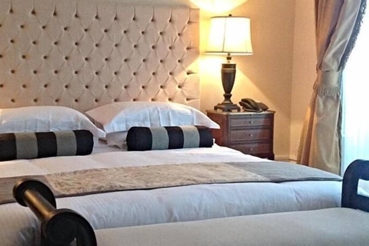 A hotel room with a tufted headboard, a bed with white bedding and striped pillows, a bedside lamp, and a telephone on a wooden nightstand.