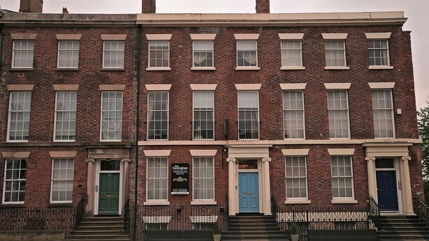 Una hilera de casas adosadas de ladrillo rojo con marcos blancos en ventanas y puertas, una puerta verde a la izquierda y una azul a la derecha.