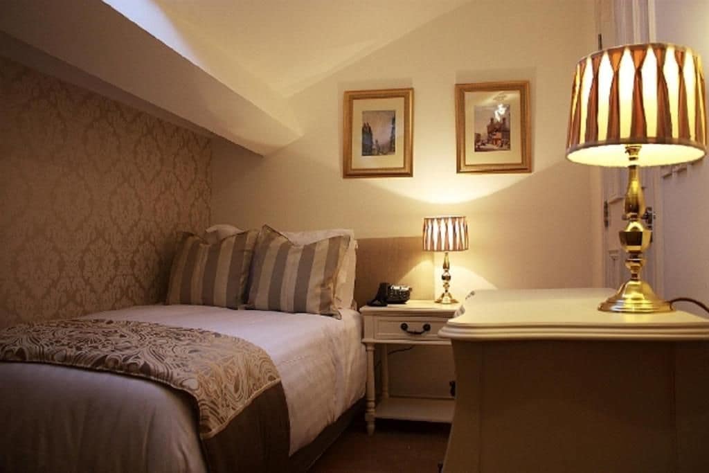 A hotel room with a bed, nightstand, lamp, and two framed pictures on the wall.