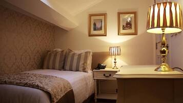 A hotel room with a bed, nightstand, lamp, and two framed pictures on the wall.