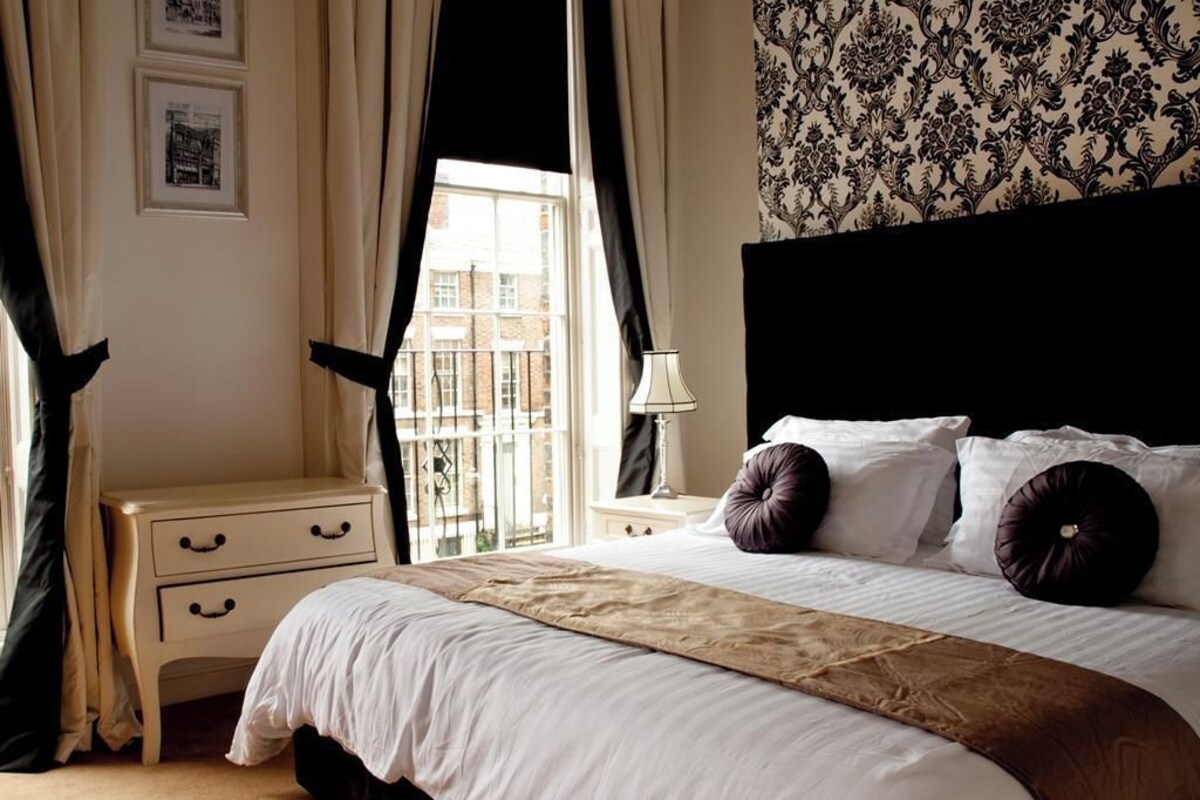 A hotel room with a bed, a nightstand, a lamp, and a window with curtains.