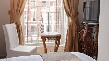 A hotel room with a bed, a chair, a small table, a television, and a view of a building through a window.