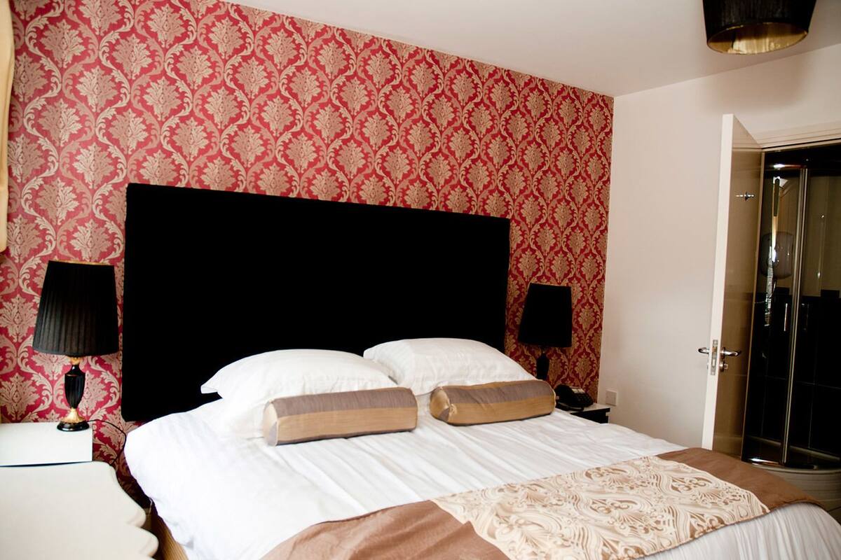 A hotel room with a large bed, two bedside tables, a black headboard, and patterned wallpaper.