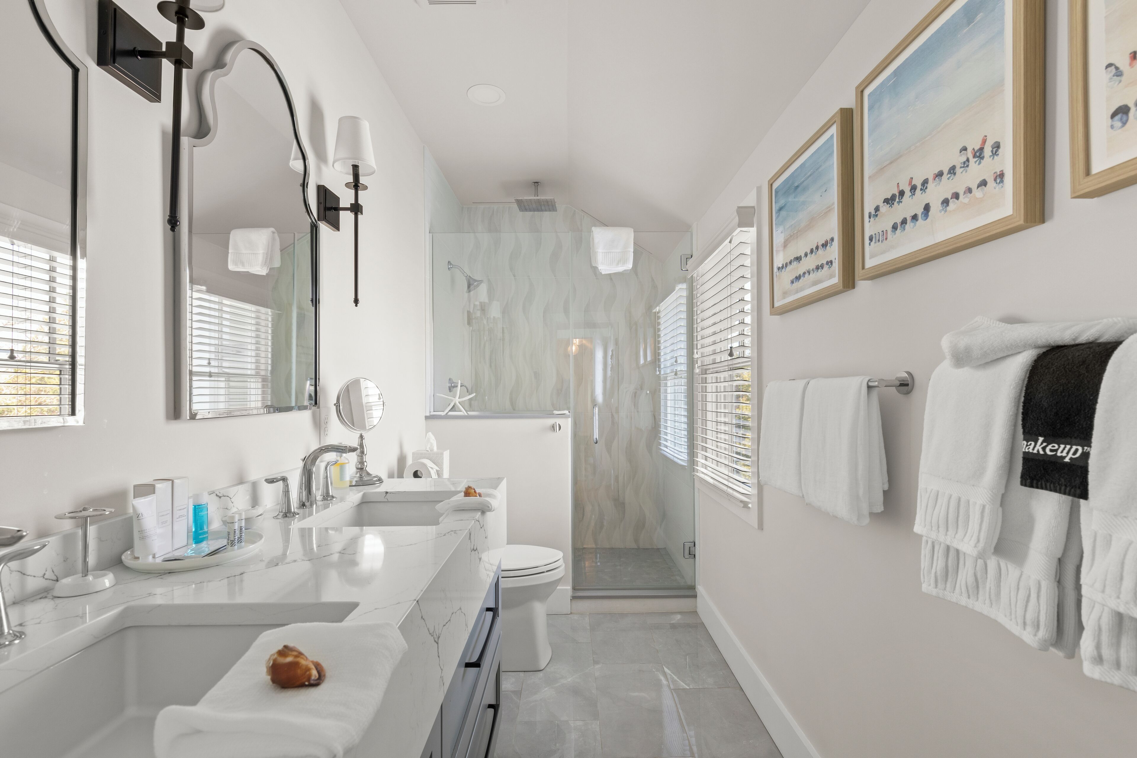 A modern bathroom with a large mirror, two sinks, a shower, and a toilet.
