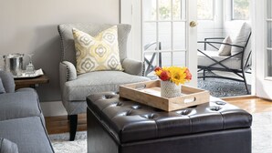 Un salón con un sillón gris, un reposapiés negro y una bandeja de madera con flores.