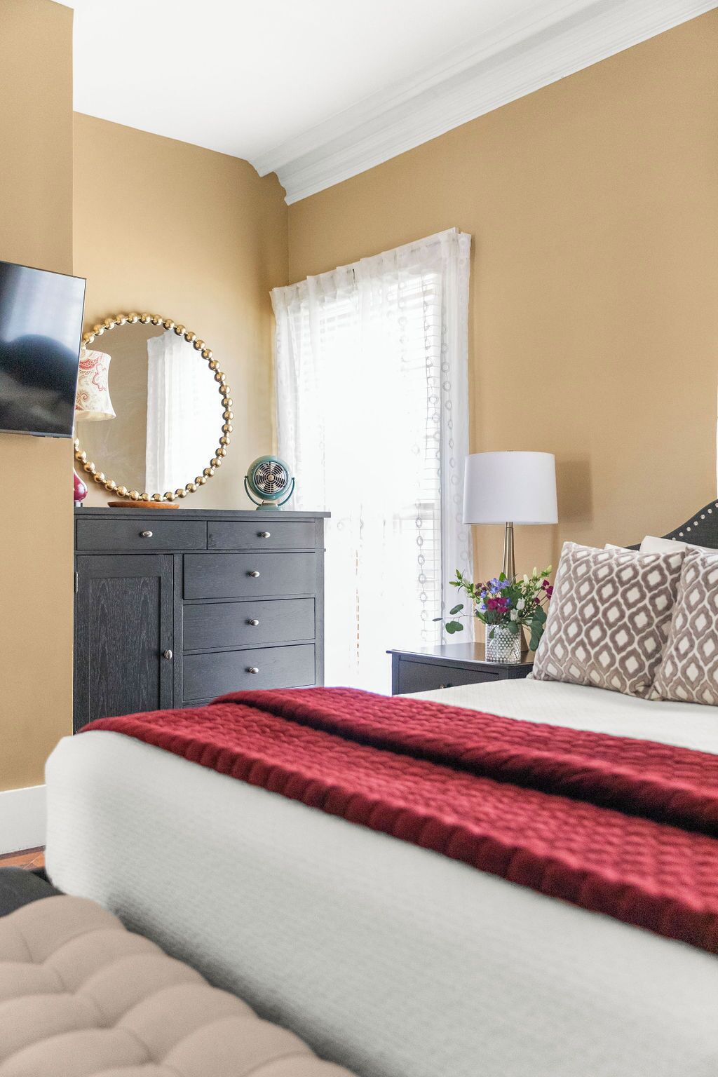 Un dormitorio con cama, cómoda, espejo, lámpara y ventana con cortinas.