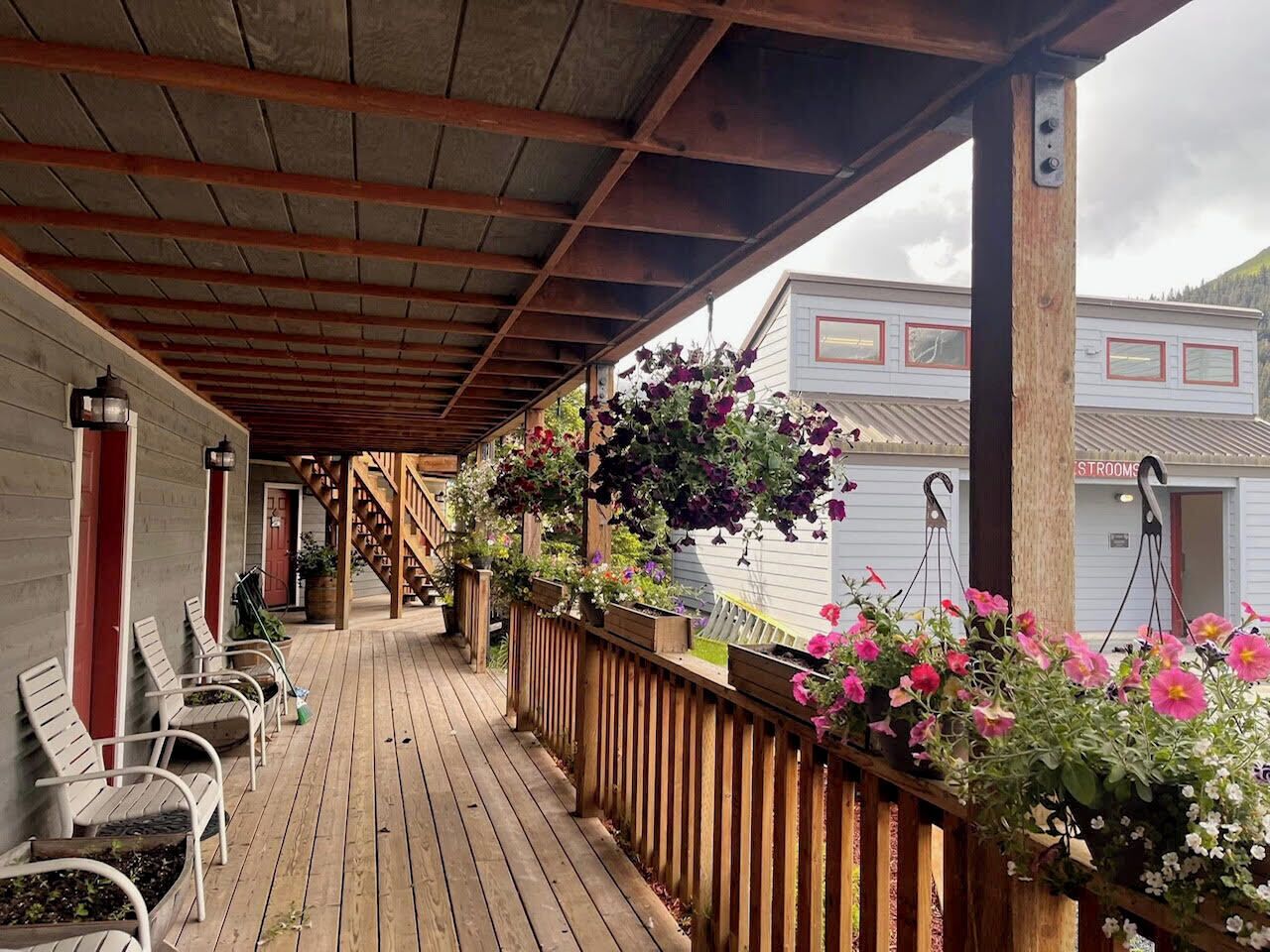 A covered porch with wooden chairs, a wooden fence, and hanging flower baskets.