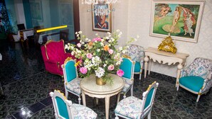 A room with a round table surrounded by four chairs with blue upholstery, a vase of flowers, and a clock on a side table.