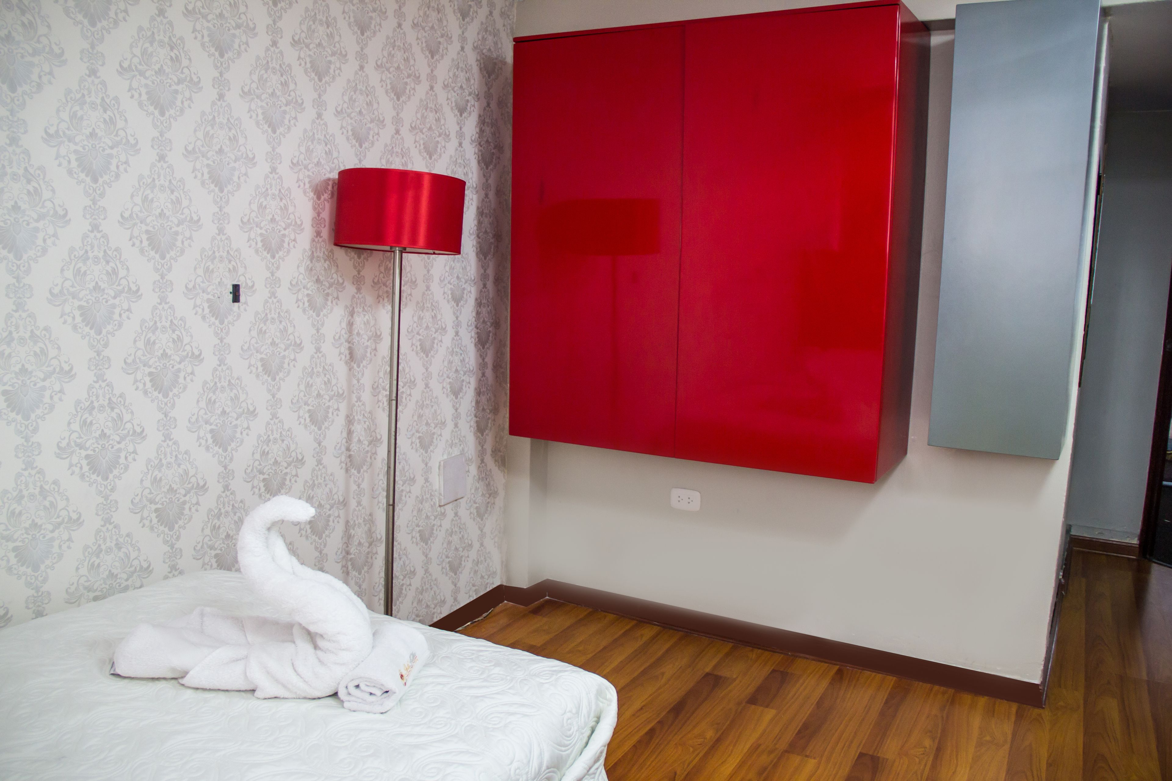 A bedroom with a bed, a red wardrobe, a floor lamp, and a patterned wallpaper.