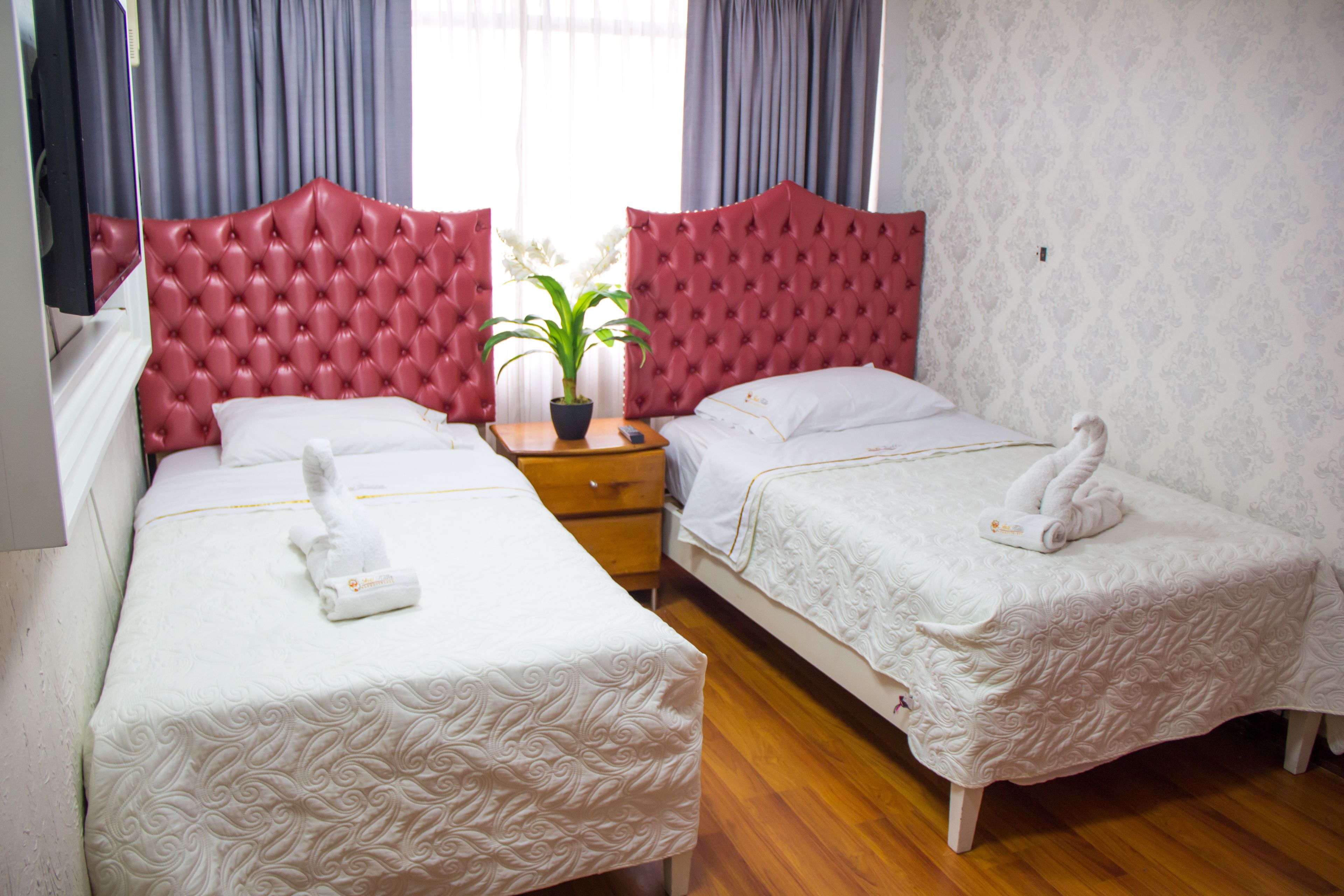 A hotel room with two beds, a potted plant, and a wooden nightstand.