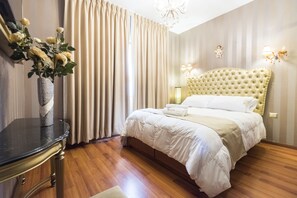 Ein Hotelzimmer mit einem großen Bett, einem Nachttisch, einer Vase mit Blumen und einer Kristallleuchter.