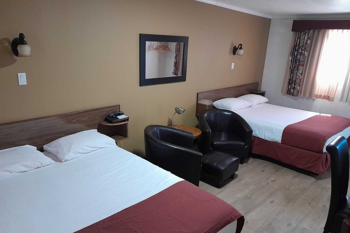 Quarto de hotel com duas camas, uma escrivaninha, uma cadeira, uma mesa de cabeceira e um espelho.
