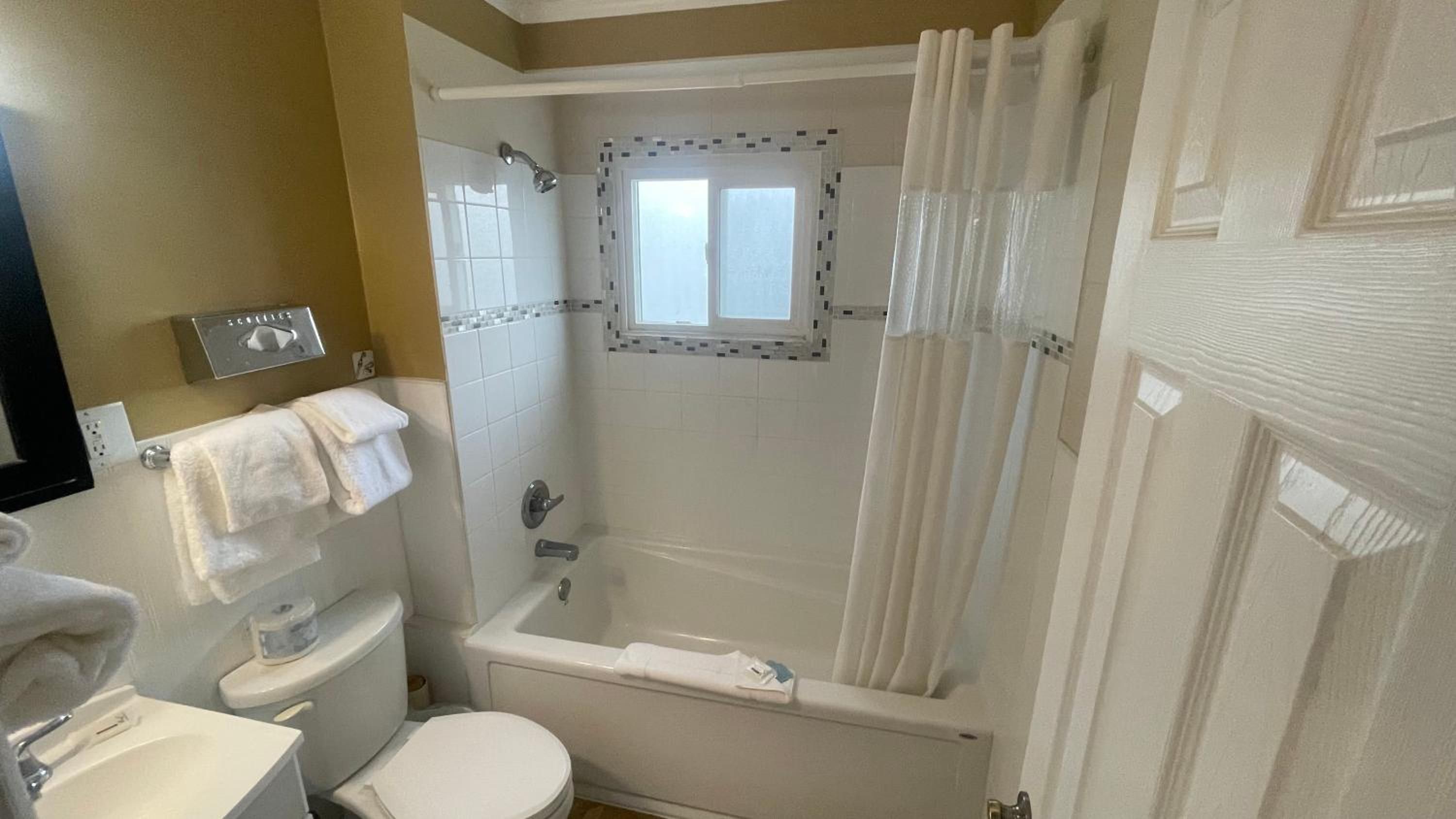 A bathroom with a toilet, sink, shower, and a window above the shower.