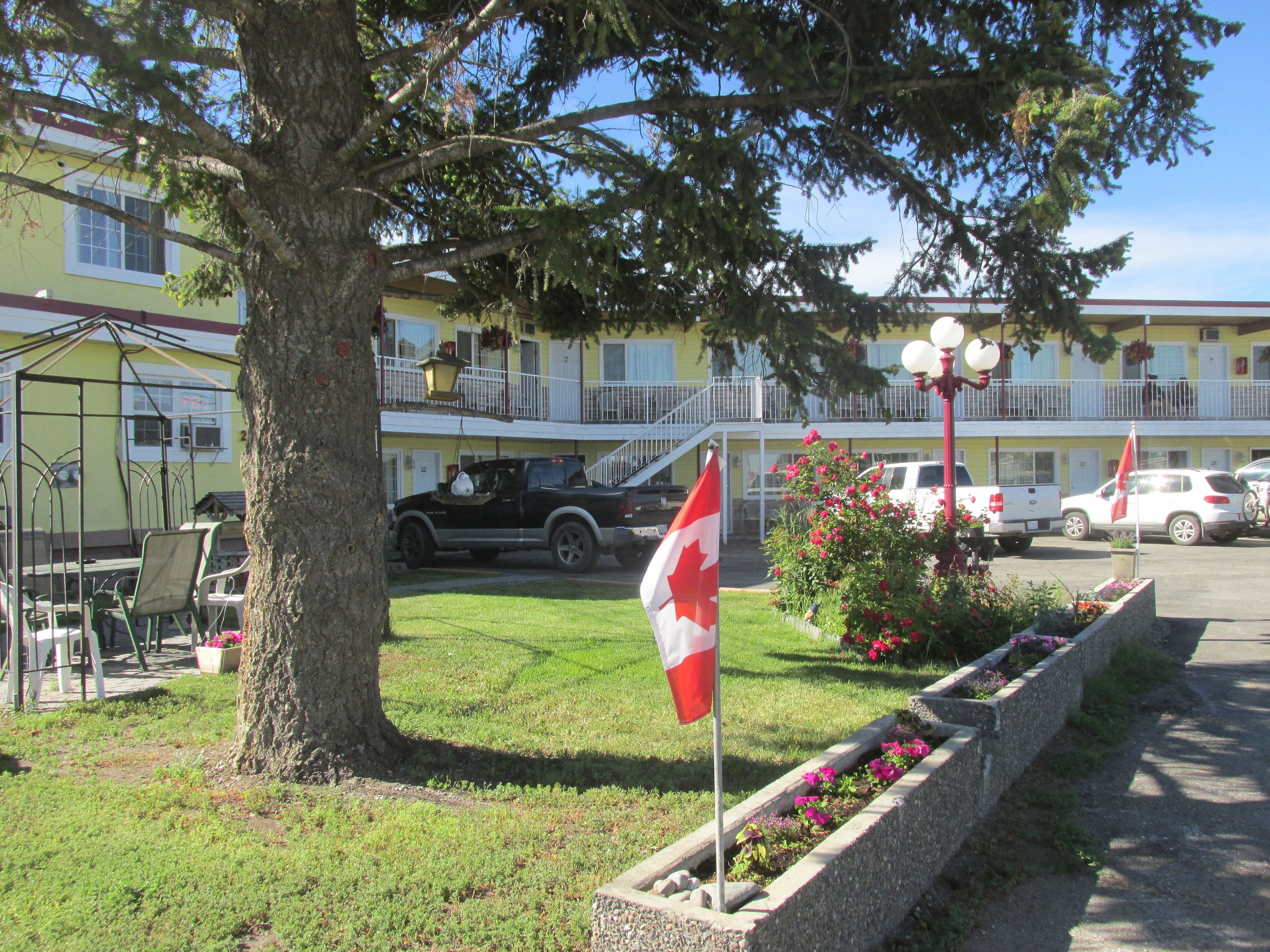A building with a yellow facade, a flagpole with a Canadian flag, and a parking area with cars.