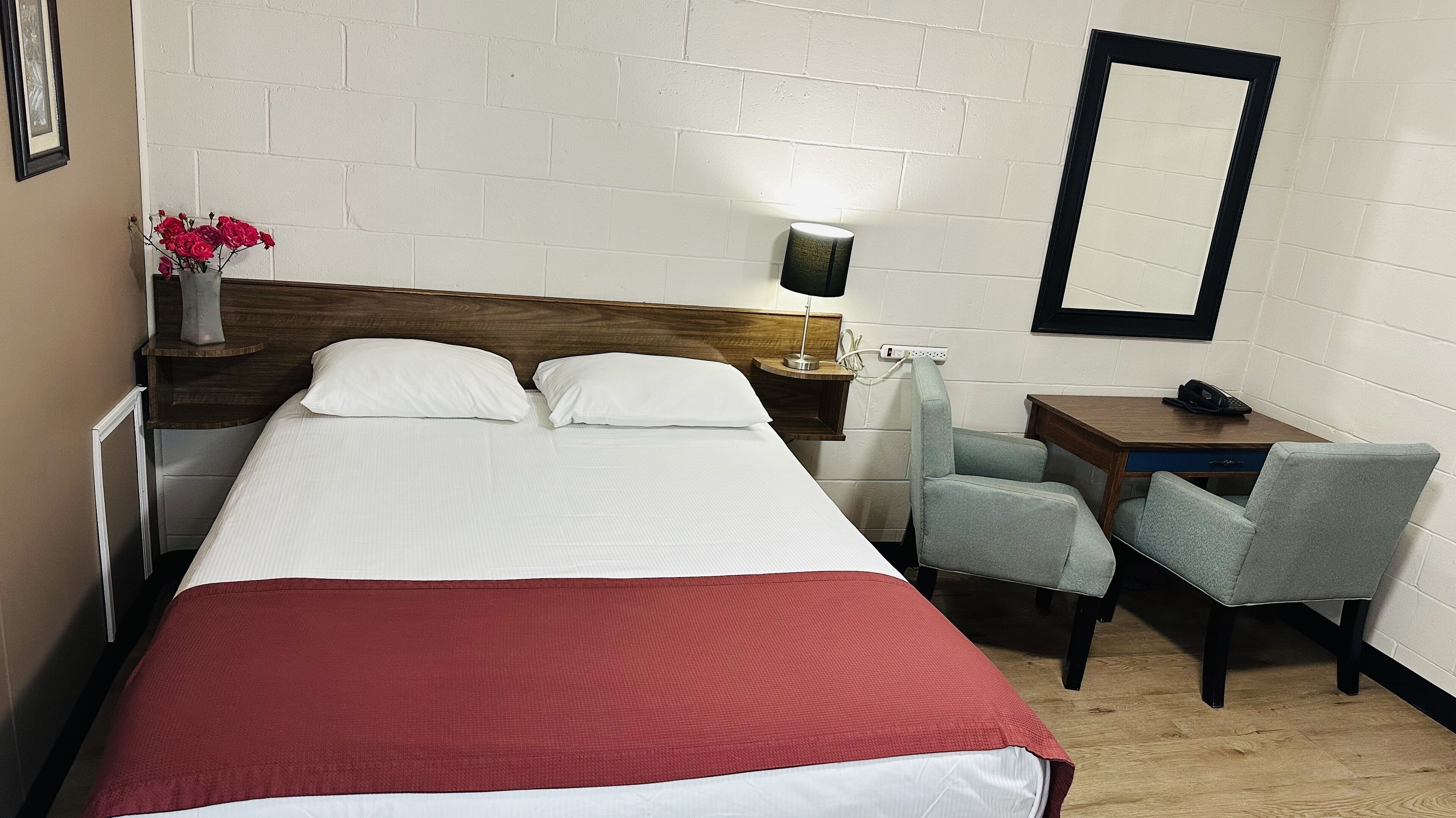 Ett hotellrum med en säng, ett skrivbord, en stol, en lampa och en spegel.