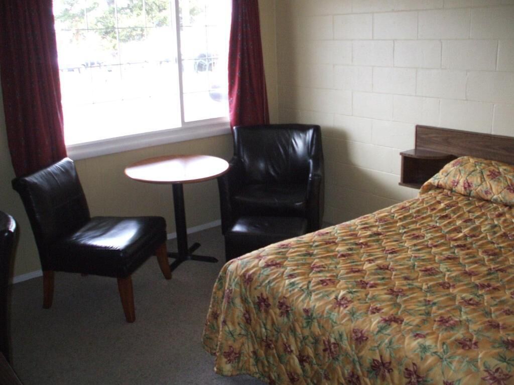 A hotel room with a bed, two chairs, a small table, and a window with curtains.