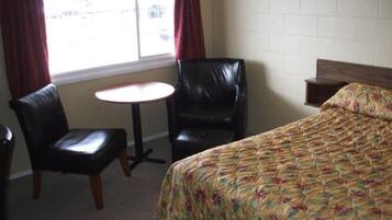 A hotel room with a bed, two chairs, a small table, and a window with curtains.