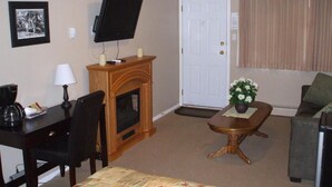 Une chambre d’hôtel comprenant un lit, un bureau avec une lampe, une télévision, une cheminée, une machine à café, un canapé et une fenêtre avec des rideaux.