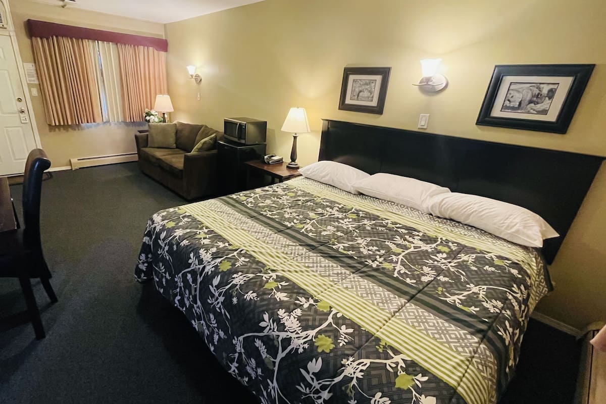 Quarto de hotel com cama, escrivaninha, cadeira, televisão e luminária.