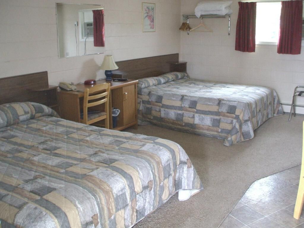 A room with two beds, a desk, a chair, a lamp, and a mirror.